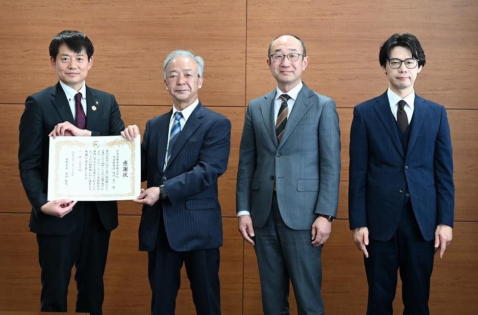 贈呈式の写真。4人の男性が並んで立っている。左側から1番目の市長と2番目の男性の方が感謝状を手に持っている。