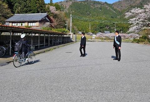 柏原中学校で、自転車に乗って通学している生徒に挨拶をしている写真