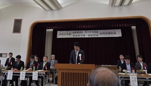 机が並べられており参加者が中央にいる男性のお話に耳を傾けているようすの写真
