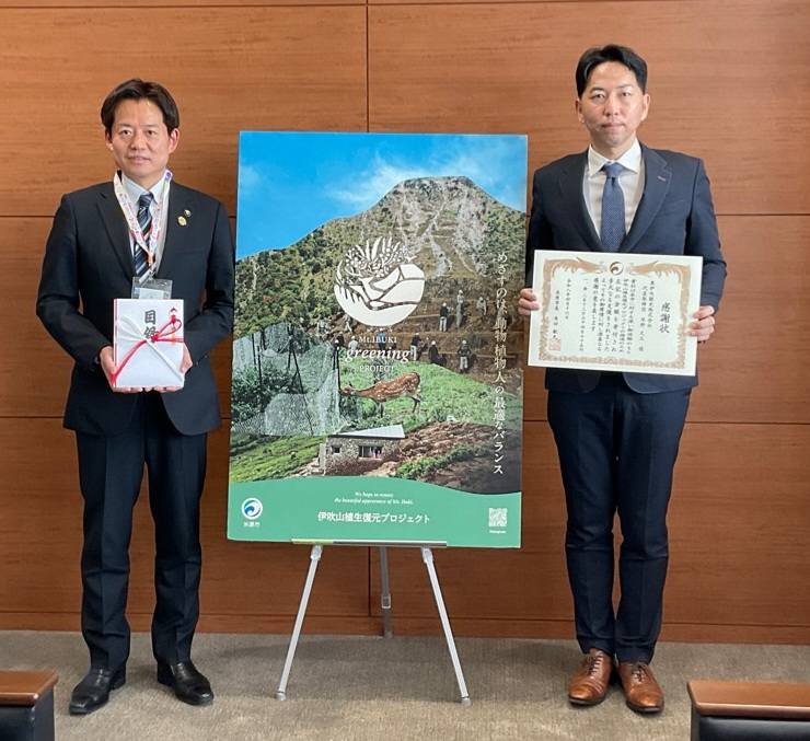 左からのし袋を持ってる市長、真ん中に伊吹山植生復元プロジェクトパネルを設置、その横には感謝状を手に持っている奥伊吹観光株式会社の方(男性)の写真