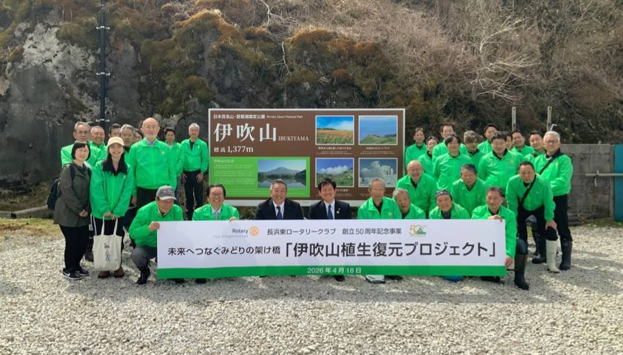 伊吹山植生復元プロジェクトと書かれた横長パネルを中心に記念撮影。緑色のウェアを着ている長浜東ロータリークラブの皆さんと市長。