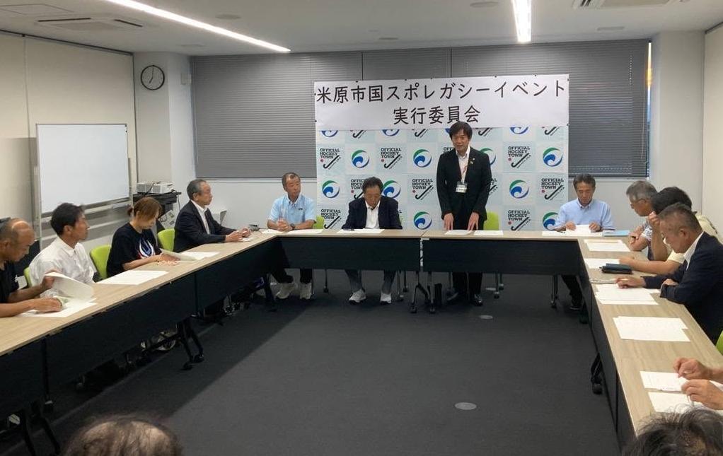 会議室にて長机で囲んで、立ってお話されている市長の写真。後ろには米原市国スポレガシーイベント実行委員会と書かれたパネルが設置されている。