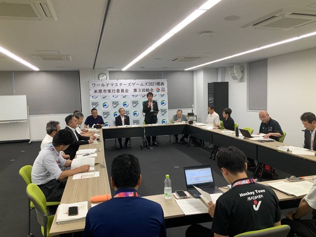 会議室にて、長机で囲み、ワールドマスターズゲームズ2021関西 米原市実行委員会とかかれたパネルが後ろにあり、マイクを手に持ちお話されている市長の写真。