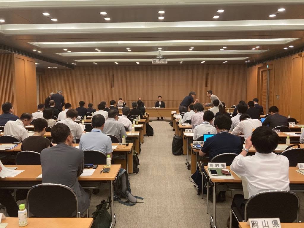会議室にて、長机で囲んで大勢の方が着席している写真