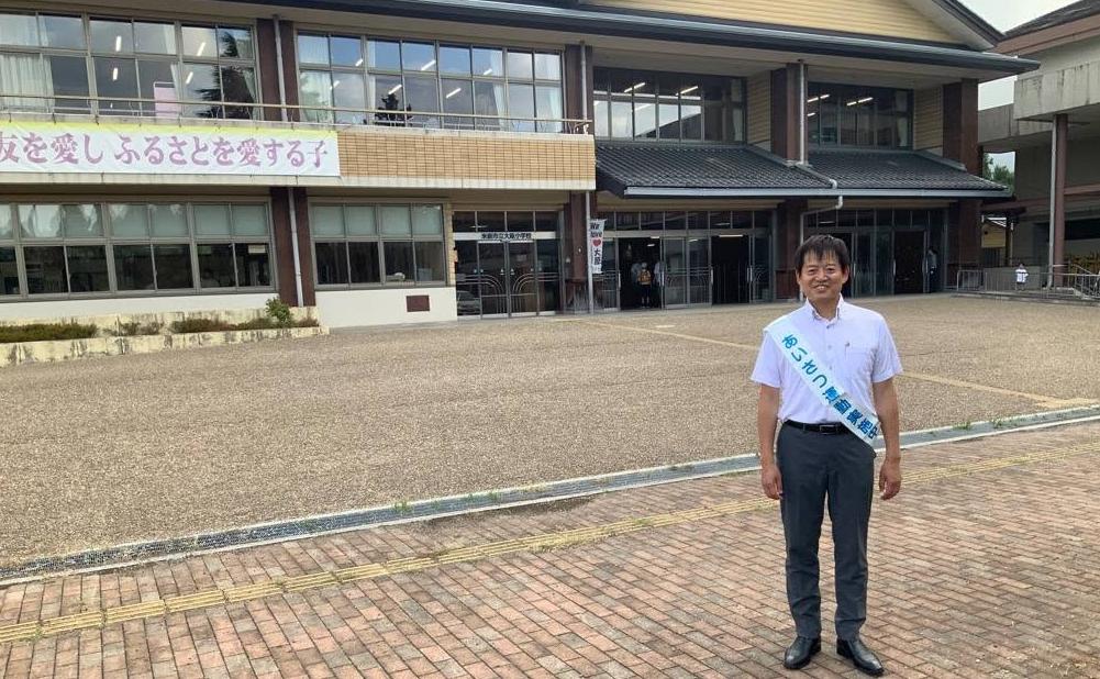 大原小学校前であいさつ運動。小学校前に立っている市長の写真。