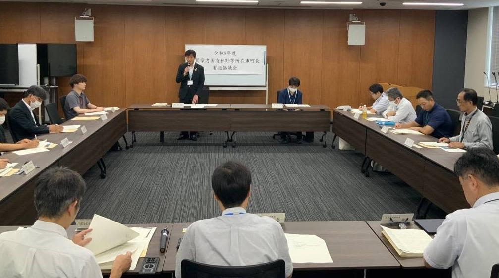 会議室にて、長机で囲んで会議しているようす。壁の手前あたりの席から立ってお話されてる市長の写真。
