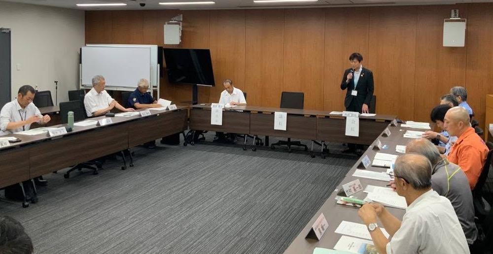 会議室にて、長机で囲んで会議しているようす。壁の手前あたりの席から立ってお話されてる市長の写真。