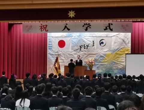 入学式全体写真。多くの人が出席しておりステージ上部に祝入学式と書かれている横断幕がある。