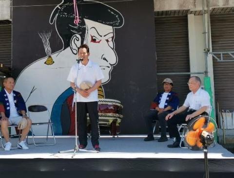 やいと祭りの看板の前で挨拶をされている市長の写真