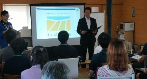 後ろに小さめのプロジェクタースクリーンがあり、挨拶をされている市長の写真