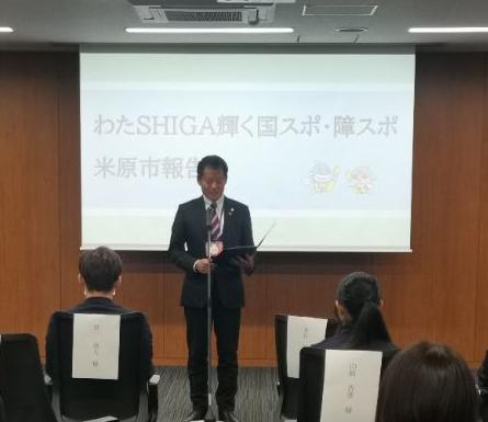 後ろにプロジェクタースクリーンがあり、わたSHIGA輝く国スポ・障スポ米原市報告会と書かれている。選手たちの前で挨拶をされている市長の写真。