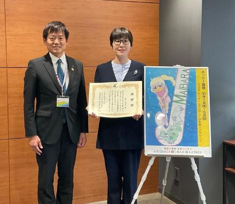 ポスターのパネル横で市長と表彰者が記念撮影しているようす