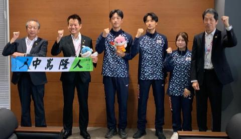 国スポ出場職員を真ん中に集合写真。握りこぶしを顔の前に持ってきて笑顔になっている皆さん。