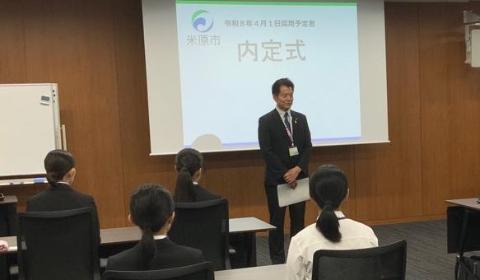 内定式と書かれたスクリーンを後ろに、採用職員の皆さまに挨拶をしている市長