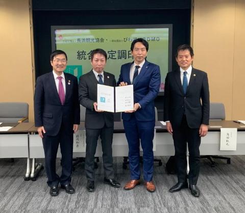 記念撮影。4人の男性がおり真ん中の2人は書類をともに手に持っており、市長は一番左の位置にいる。