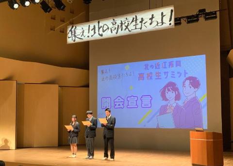 ステージ上で3人の高校生たちが開会宣言を行っている様子