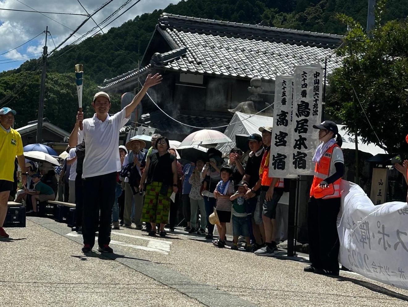 右手で炬火トーチを持って、左手で手を振りながら笑顔で走る米原市角田航也市長の写真。