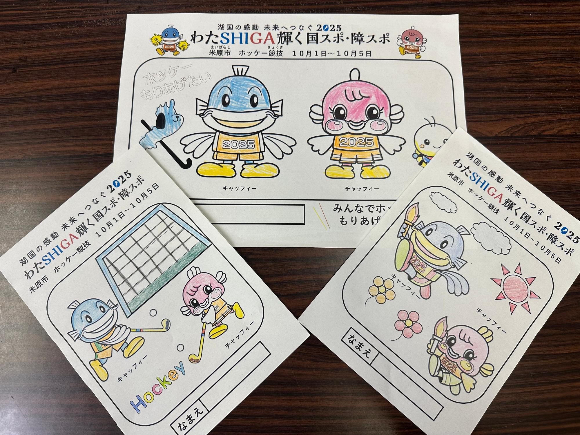 米原市ホッケー競技の啓発品塗り絵の見本画像。真ん中にあるぬりえ見本はキャッフィー、チャッフィー、ほたるん、しがけんが並んでいる絵。左のぬりえ見本はキャッフィーとチャッフィーがホッケーをしておりゴールに向けてボールを入れている絵。右のぬりえ見本は周りに太陽とお花があり、キャッフィーとチャッフィーそれぞれ聖火をともしたトーチを手に持って走っている絵。
