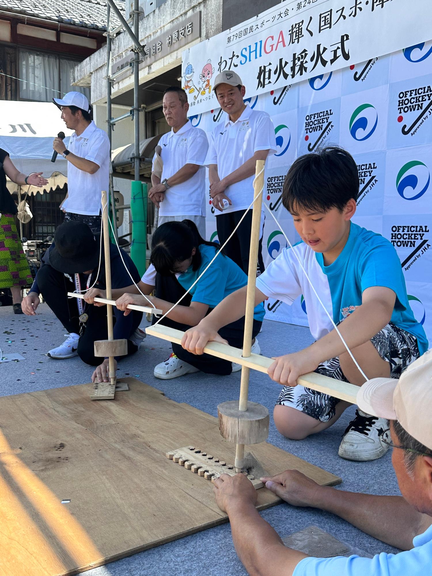 柏原やいと祭りのステージにて、まいぎり式で火おこしをして採火をするやいとキッズの小学生2人の画像