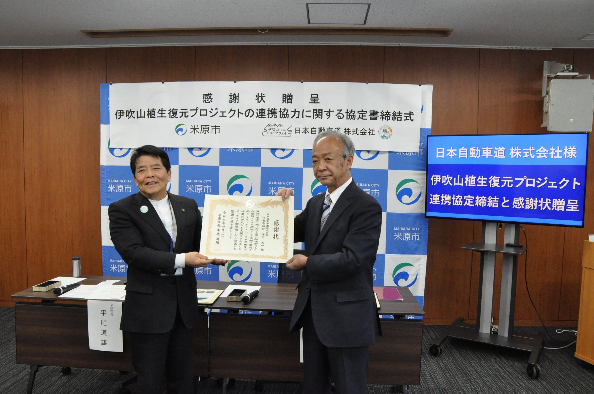 感謝状の贈呈のようす。市長と男性の方が感謝状を手に持っている。
