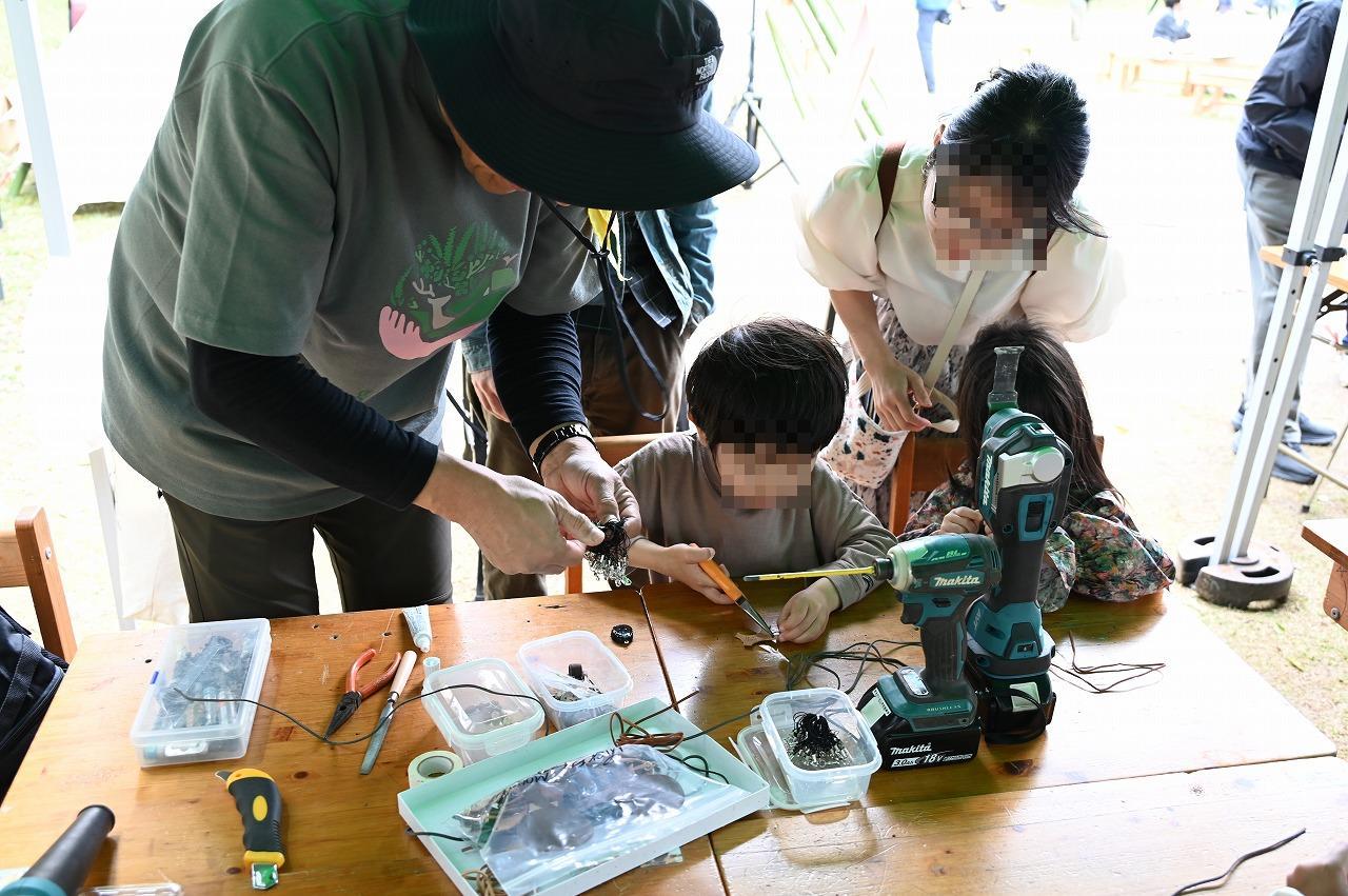 男の子が指輪作りで道具を使って金属を曲げていてをそれを手助けしているスタッフの写真