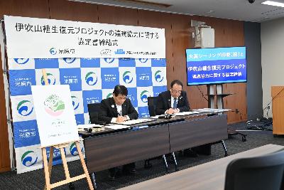 大阪シーリング印刷株式会社との連携協定締結時の写真。市長と男性の方が卓上で紙に何かを書いているようす。