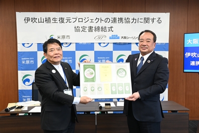 ロゴステッカーの贈呈の写真。市長と男性の方が額縁に入っているロゴステッカーを手に持っている。