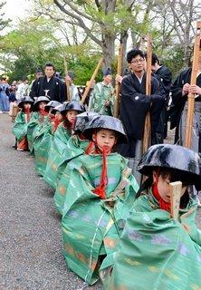 竹を持った袴姿の男性と、黒い笠をかぶり緑の服をまとった8人のこどもたちの写真