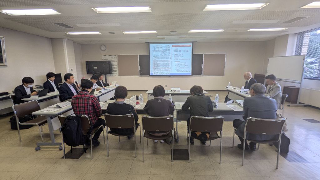 第3回審議会の開催風景。会議室正面に資料を投影し、事務局から委員に説明している様子。