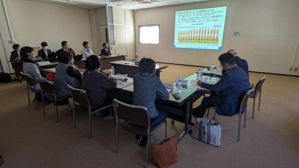第5回審議会の開催風景。会議室正面に資料を投影し、事務局から委員に説明している様子。