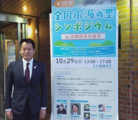 第17回全国水源の里シンポジウムのポスター横で、記念撮影をされている市長の写真