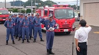 消防ポンプ車の横に整列する消防団員と敬礼する市長の写真