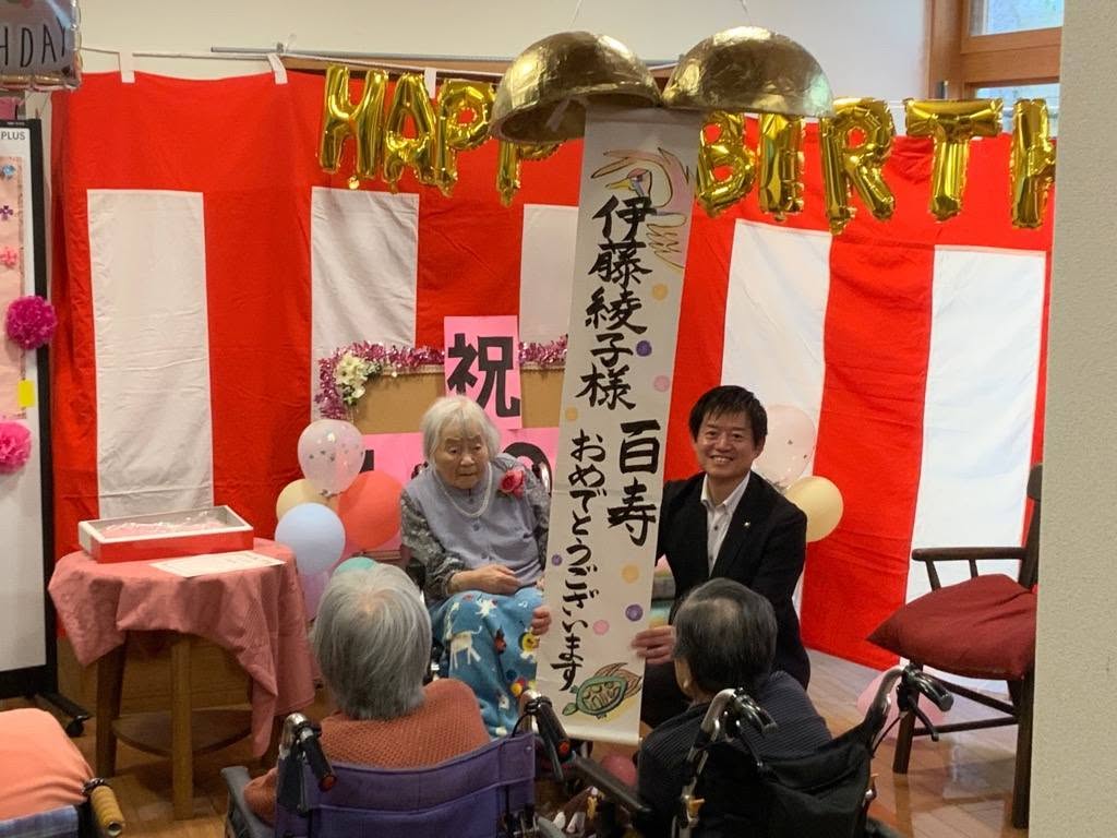 100歳のお祝い会で、100歳を迎えられた市民さんとお祝いしている市民たちと市長の写真