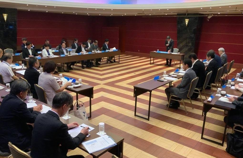 会議室にて、大勢の方が着席しており、奥あたりの席から立ってお話されてる男性の写真