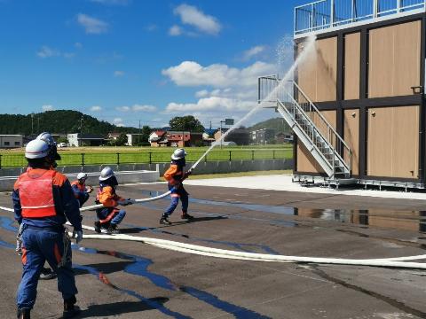 消防隊員が建物に向かってホースで放水している訓練の写真