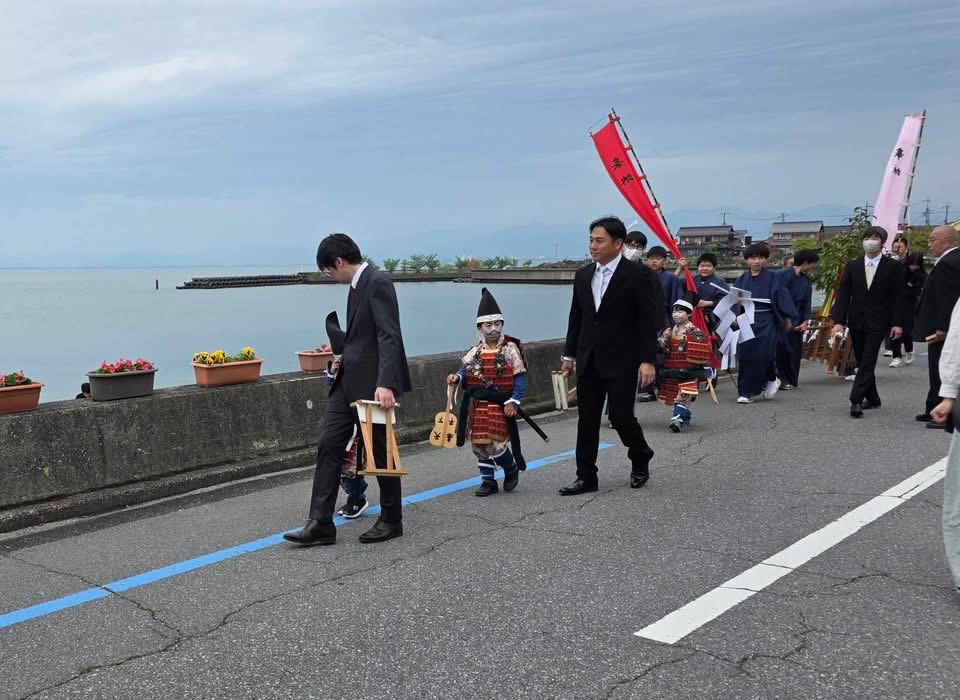磯武者行列のようす。武士の恰好をしたこどもとスーツを着ている男性2人組が集団となって練り歩いているようす