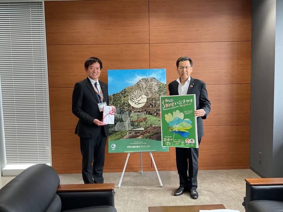 左から、のし袋を手に持っている市長、真ん中に伊吹山植生復元プロジェクトのパネルを設置、その横には株式会社エフエム滋賀の方(男性)がポスターを手に持っているようすの写真