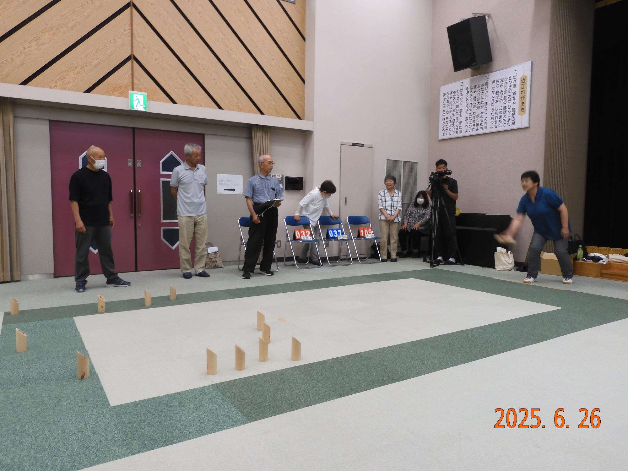 1人の男性が、木製のピン(スキットル)に向かって木の棒(モルック)を投げているようす
